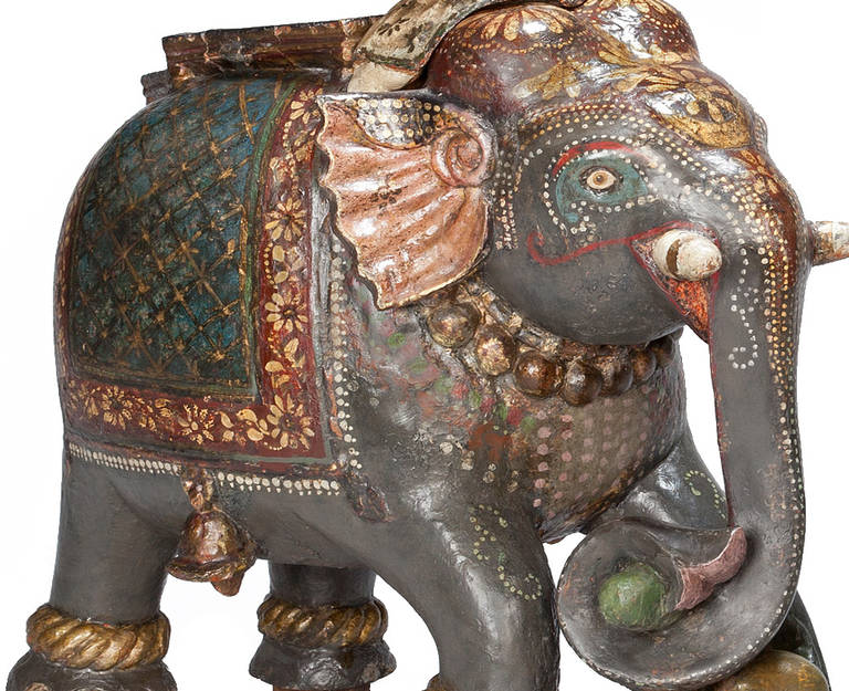 A pair of mid-19th century carved ornamental elephants, their bodies painted with faux pearls, flowers and beads their heads with floral comparisons and their backs with stylized rugs adorned with bells, their feet and husks with gold bangles, each