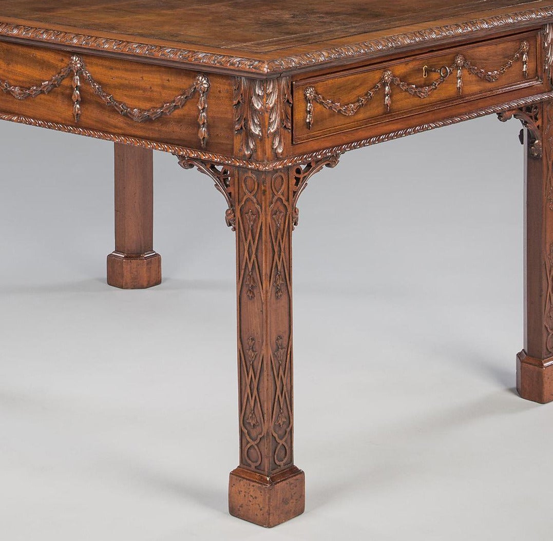 A George III mahogany library table of small-scale and rich color, the leather-lined top with carved moulded edge, the frieze having two end drawers enriched with swags of carved husks suspended from rosettes and finished with a band of gadrooned