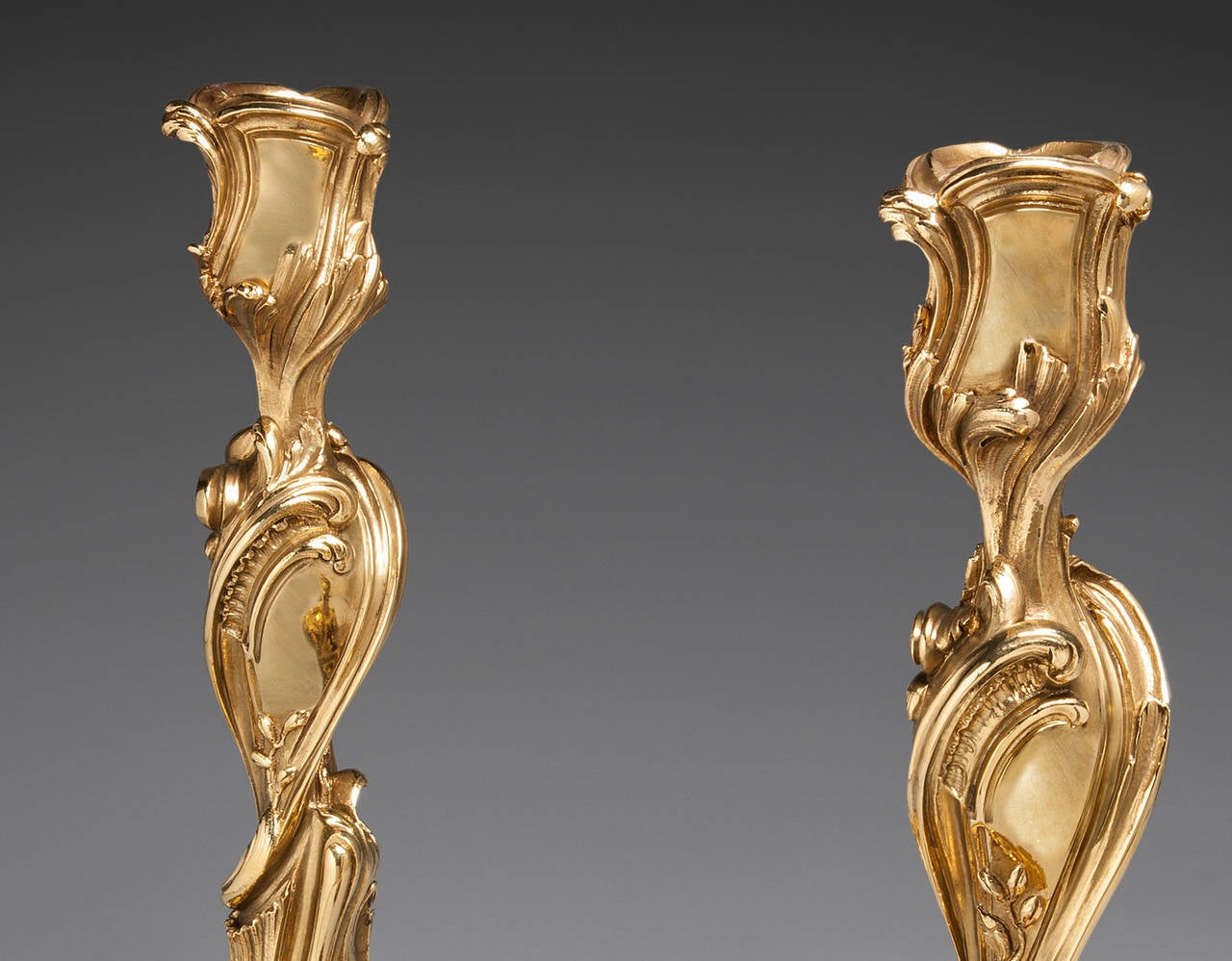 A pair of mid-19th century Rococo Revival gilt bronze candlesticks in the Louis XV style, the bold scrollwork and naturalistic sprigs of foliage reminiscent of the designs of J.-A. Meissonier.