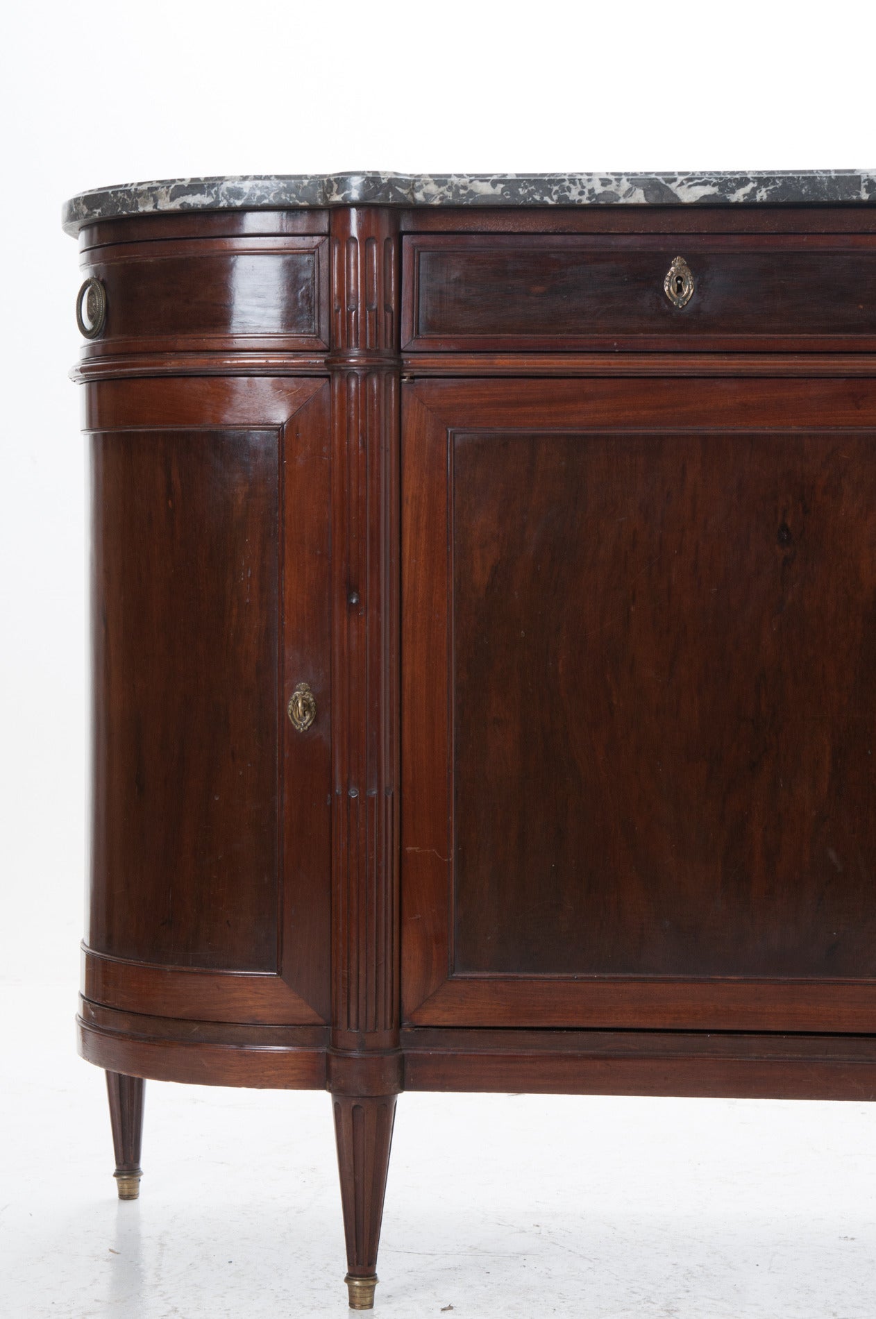 Elegant French Louis XVI demilune dark mahogany enfilade or buffet with its original shaped black marble top. Classic lined top center drawers with fluted legs, appear to begin just under the marble. Side drawers and doors curve to open, the whole