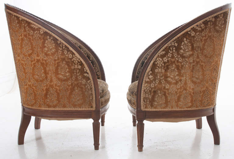 A pair of comfortable French Louis XVI bergeres. Walnut wood frames with barrel-backs, down swept arms, ending in classic fluted front feet. The upholstery is original to the chairs, needing to be reupholstered. 1880 or earlier.