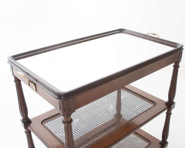 Darling French serving table with a mirrored top meant to look like a tray with brass handles. Turned mahogany table legs support this table with two more shelves featuring cane, in good condition. 1920's