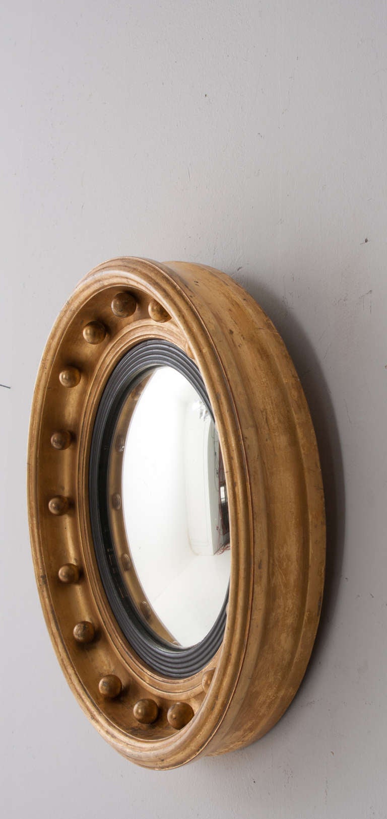 English convex mirror with gold gilt molded frame featuring round gilt balls, black ebonized and reeded frame holds in the mirror glass, 1920.