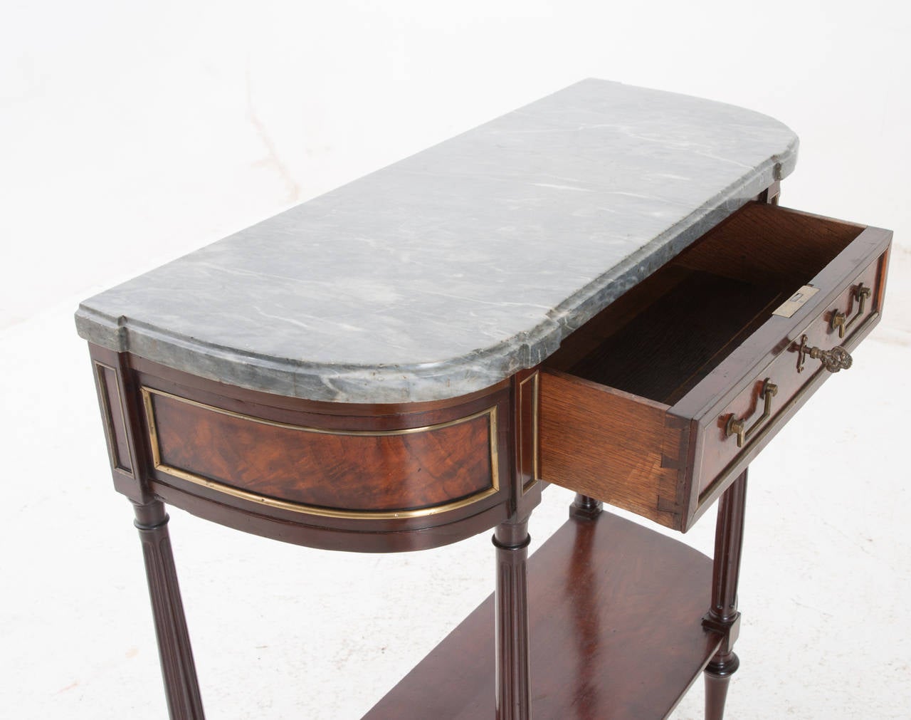 A petite console table in the Louis XVI taste with its original shaped gray marble top. The mahogany base is darling with burl mahogany veneer paneling around the apron, accented with brass banding. A single drawer is found in cleaned working