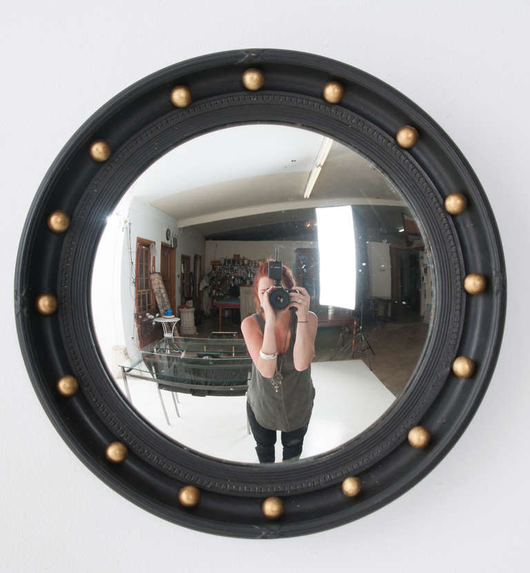 Convex mirror with carved ebonized frame featuring round gilt balls, black ebonized reeded frame holds in the mirror glass.