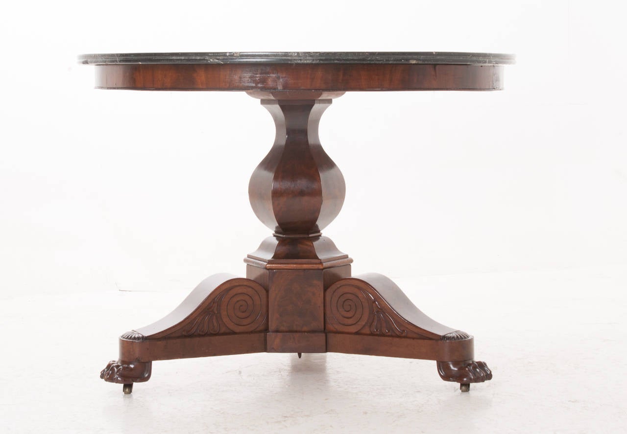 French Restauration period center table from the 1820s. Original fossil marble sits over the mahogany table base with finely figured burl mahogany. The pedestal leads down to three legs with all end with paw feet over casters.