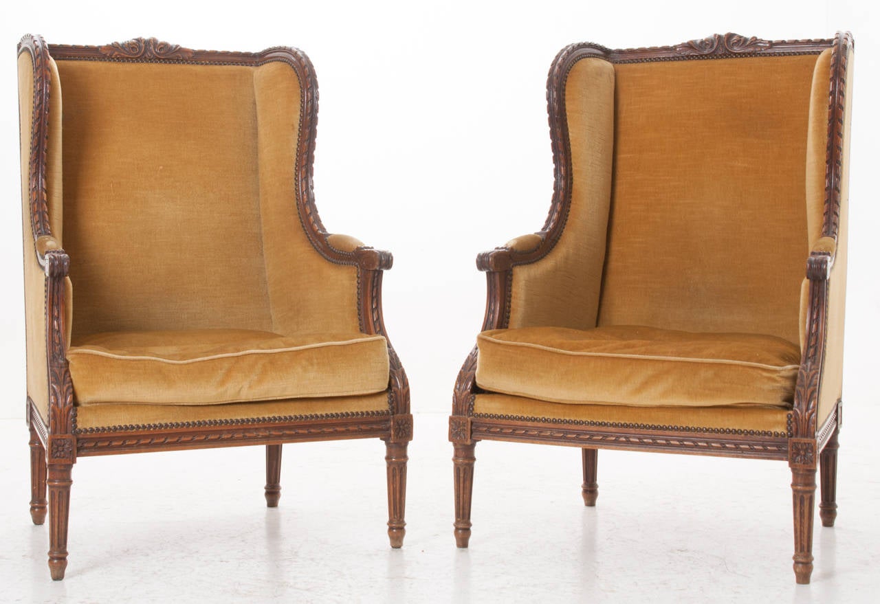 A gorgeous pair of elegantly carved walnut wingback bergeres with a used golden fabric. Be sure to see all the detail photos! This pair of chairs needs to be reupholstered and tightened before use, 1850s.