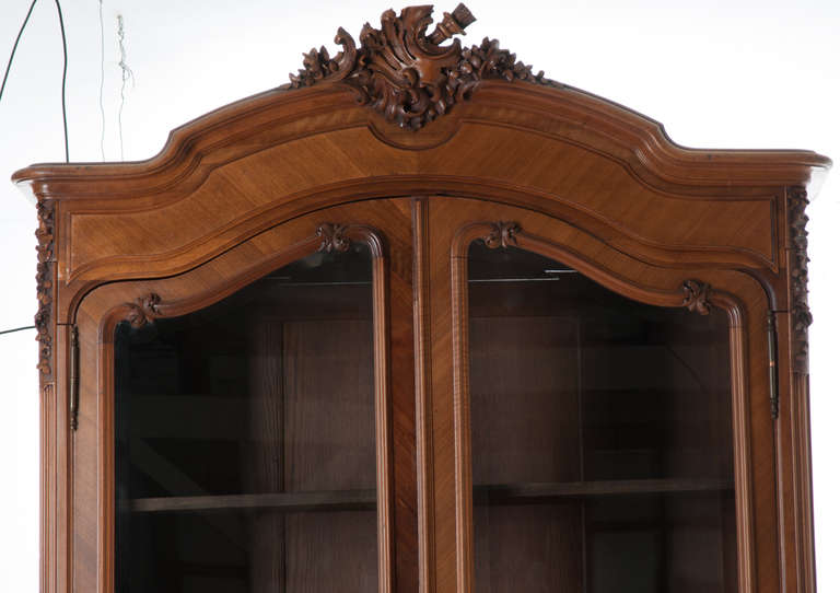 A walnut Louis XV style armoire from France, circa 1900 - 1920. Topped with a carved Rococo cartouche, above two beveled de-silvered mirror doors, opening to three adjustable shelves and two interior drawers, over a scrolling apron and cabriole