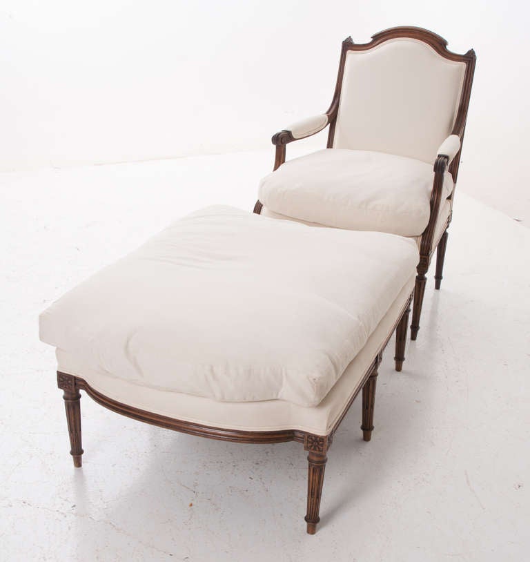 French two-piece duchesse brisee or 'chaise longue in two parts' having one fauteuil and an ottoman that fits the curve of the chair front. All walnut carved with fluted legs and rosettes, soft inviting white upholstery with a few stains,