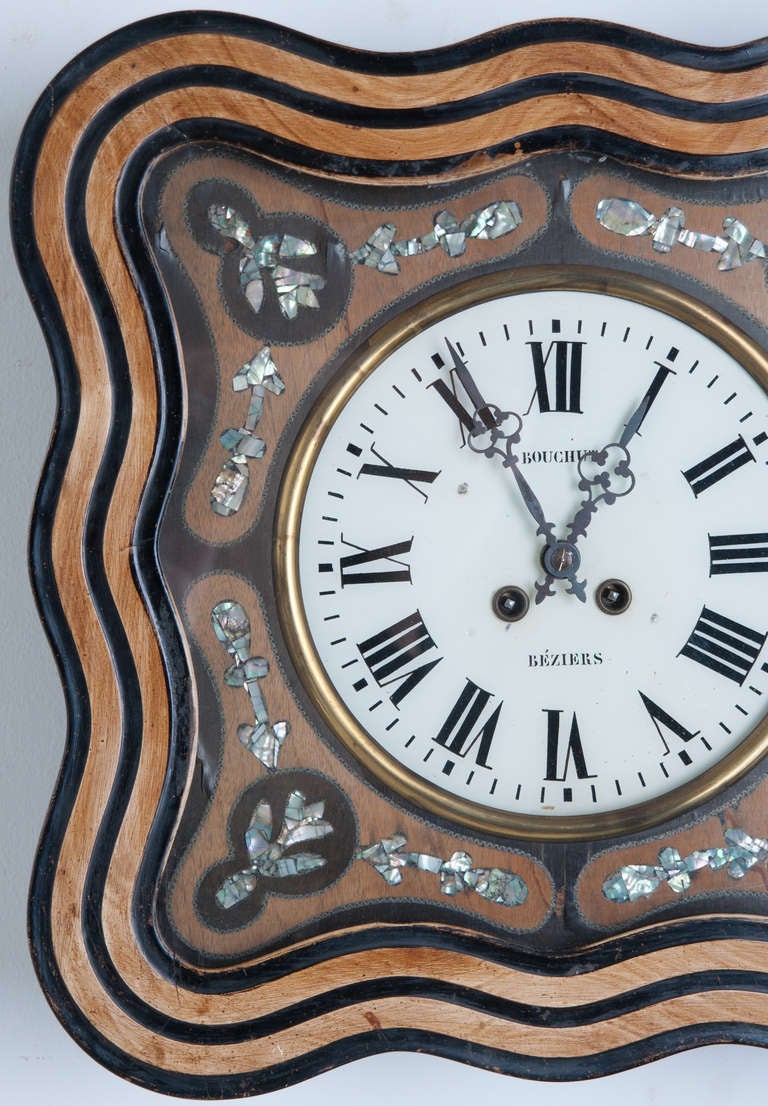 This 19th century clock is stunning with it's square rippling clock frame of ebonized and painted wood. Mother of pearl designs are inlaid in mahogany and ebonized wood, surrounding the glass clock face in symmetrical forum. Clock face reads