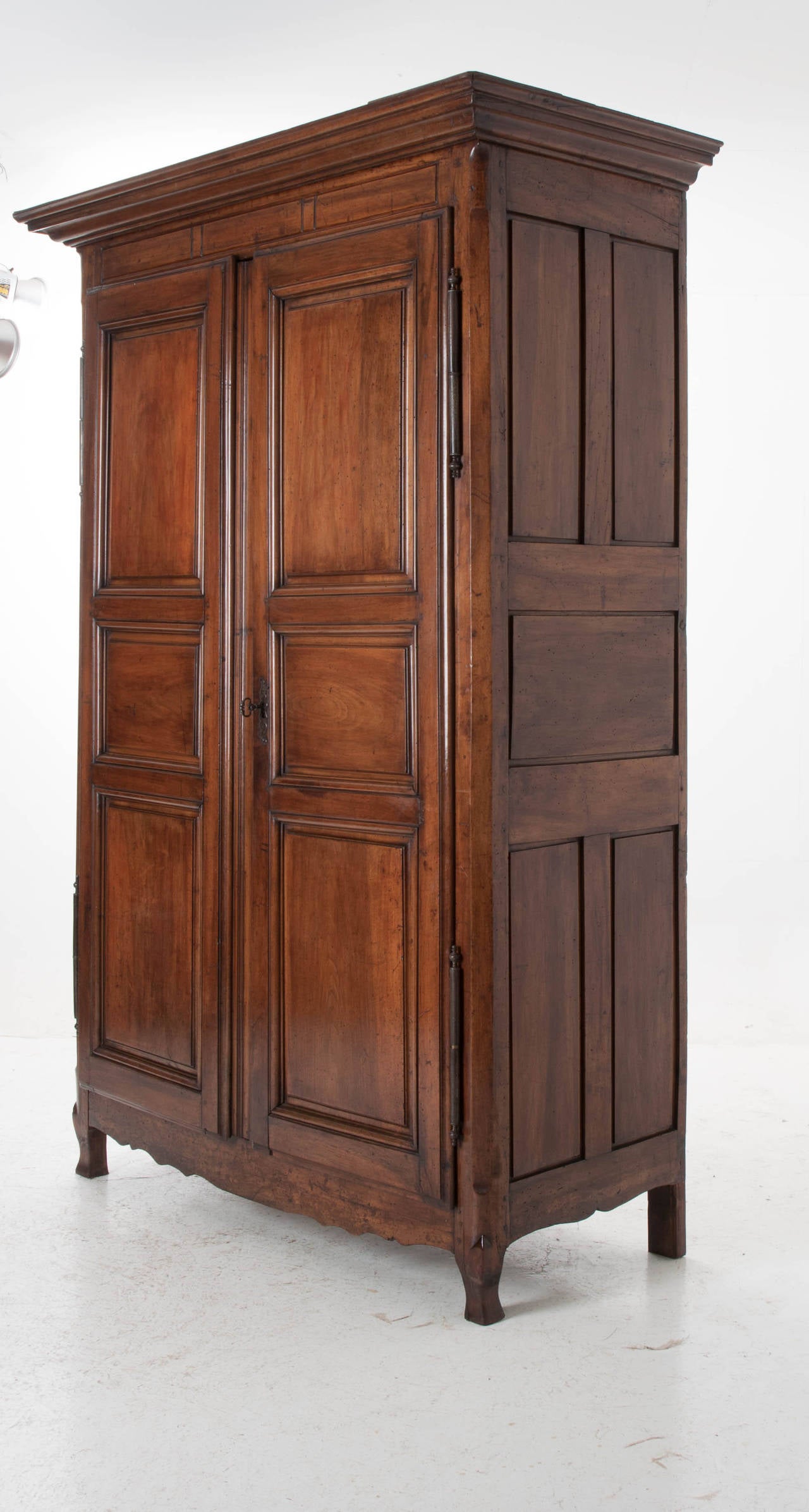 A massive scale armoire with deep carved and paneled door fronts and sides. The large doors open on steel barrel hinges with all its original locking mechanisms and large skeleton key. This armoire retains its beautiful, rich, original color and