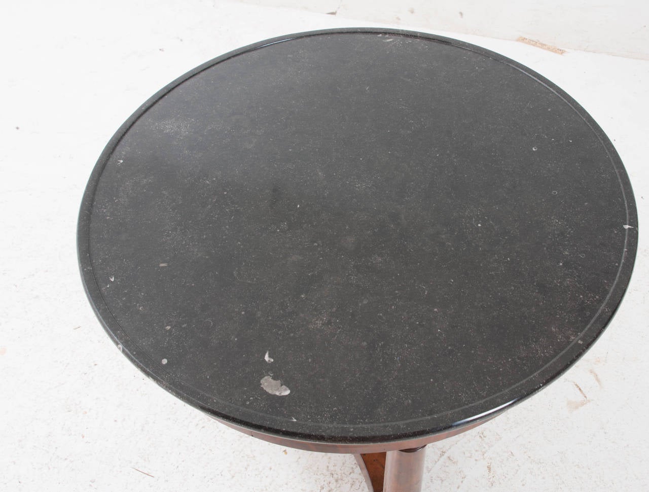A gorgeous round Empire center table with its original black fossil marble top over a flame mahogany apron over three column legs and ending with a shaped stretcher base and metal casters. Make sure to go over the pictures carefully, the veneering