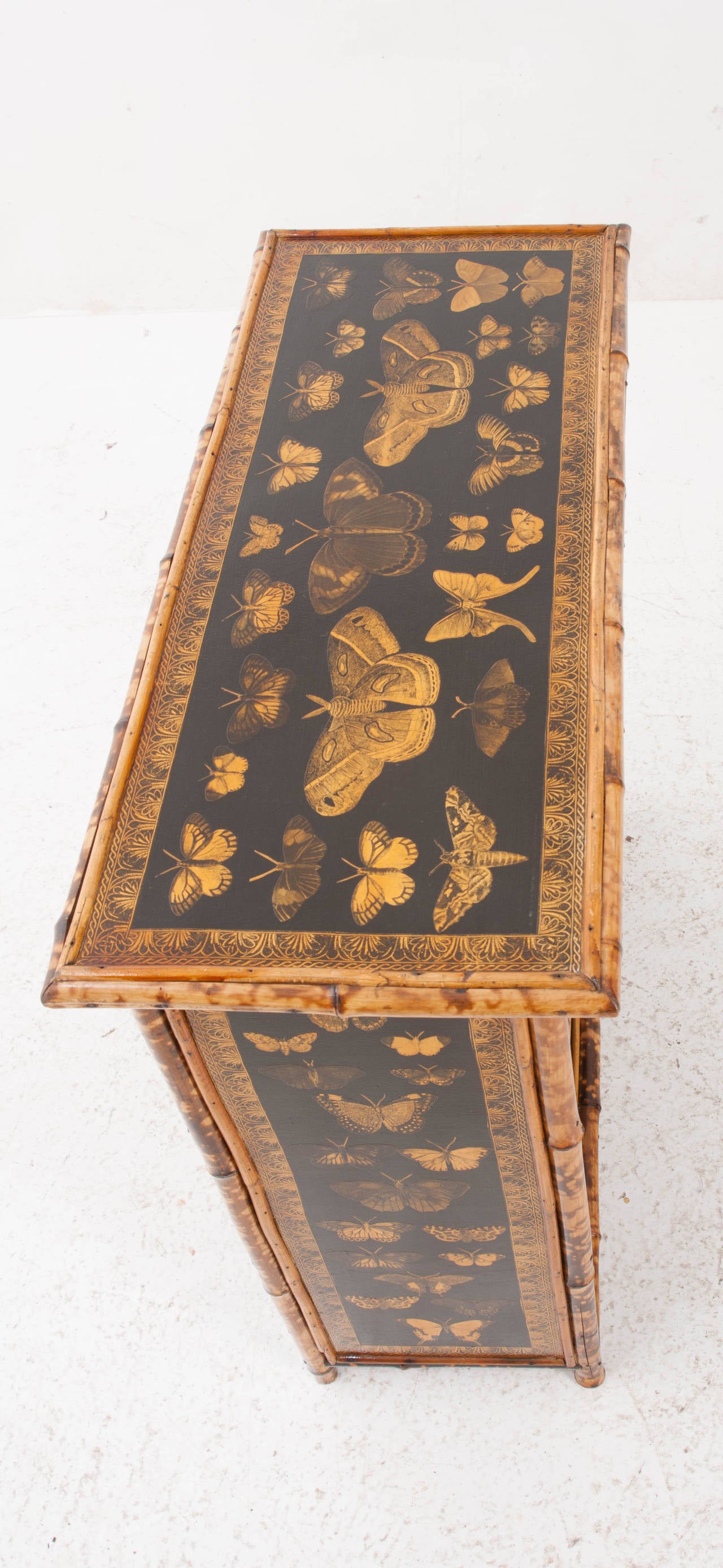 English bamboo bookshelf from the 1890's has been recently refinished. Where you see black paint and decoupage is where seagrass would have been. The seagrass has been damaged and replaced with this fabulous butterfly decoupage and interesting