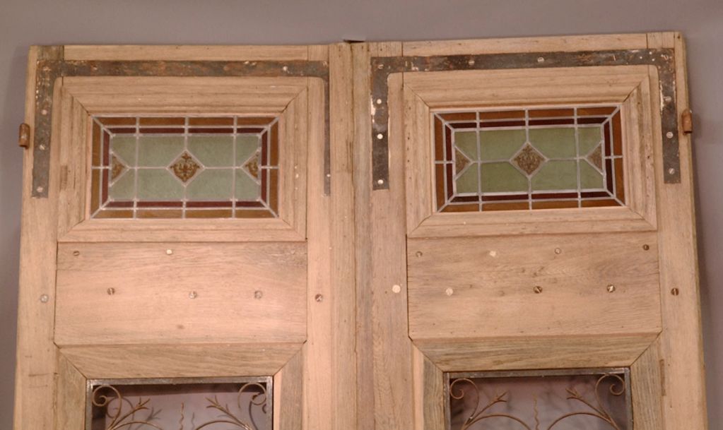 French oak double doors with iron gills and stained glass transoms. door are sitting in front of gray paper so the colors of the stained glass are not as shown. Example the red looking stained glass is really yellow. There is no glass behind the