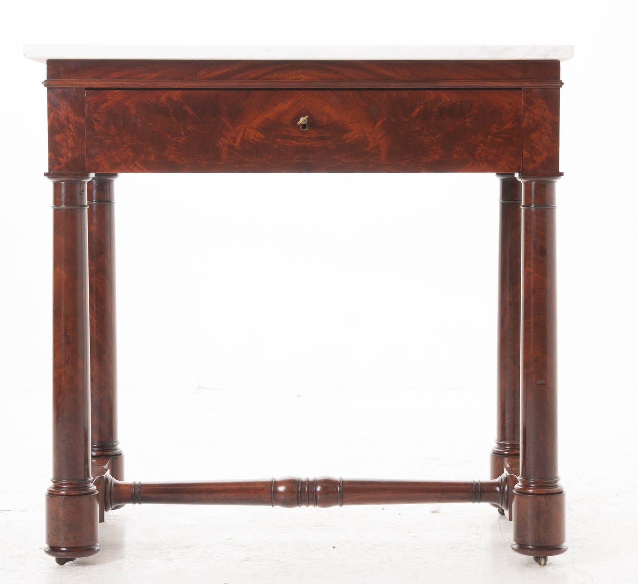 A stunning English flame mahogany side table with a white marble top. There is a single fitted drawer in the apron over four cylinder legs connected with a stretcher, the whole on its original casters, 1880s.