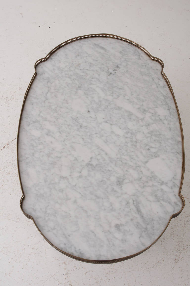 A fabulous example of the Louis XVI style made in the 1950s. White marble is inset in the walnut base with a brass pierced gallery. The apron of this table holds two drawers and two drink slides, tapered and fluted table legs end in brass caps.