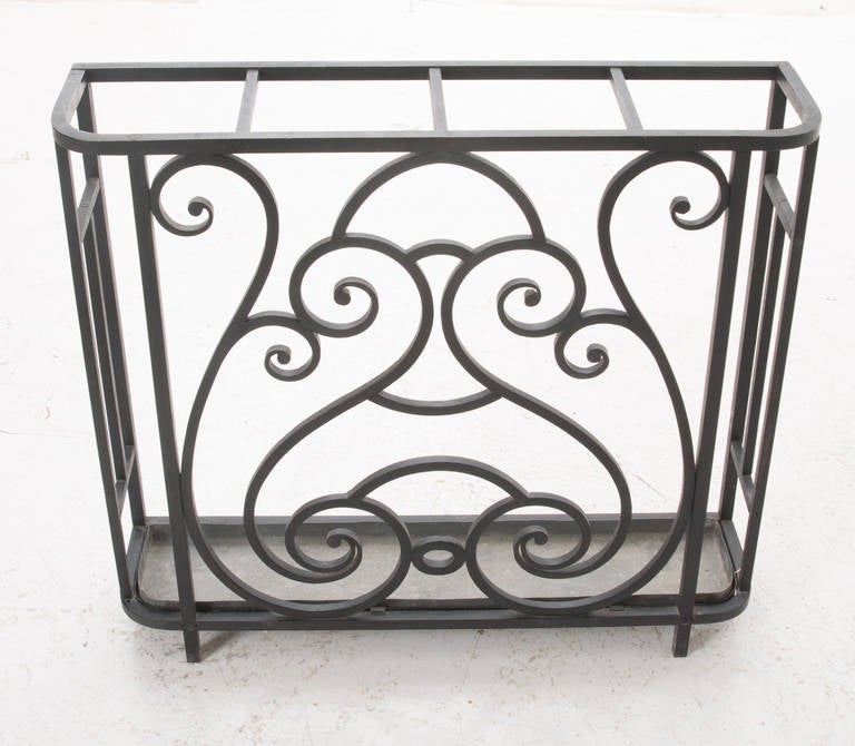 A darling umbrella stand with square, flat edge iron in whimsical designs, similar to a stairway railing or iron gate. Tole removable drip pan is in tact, 1920s.