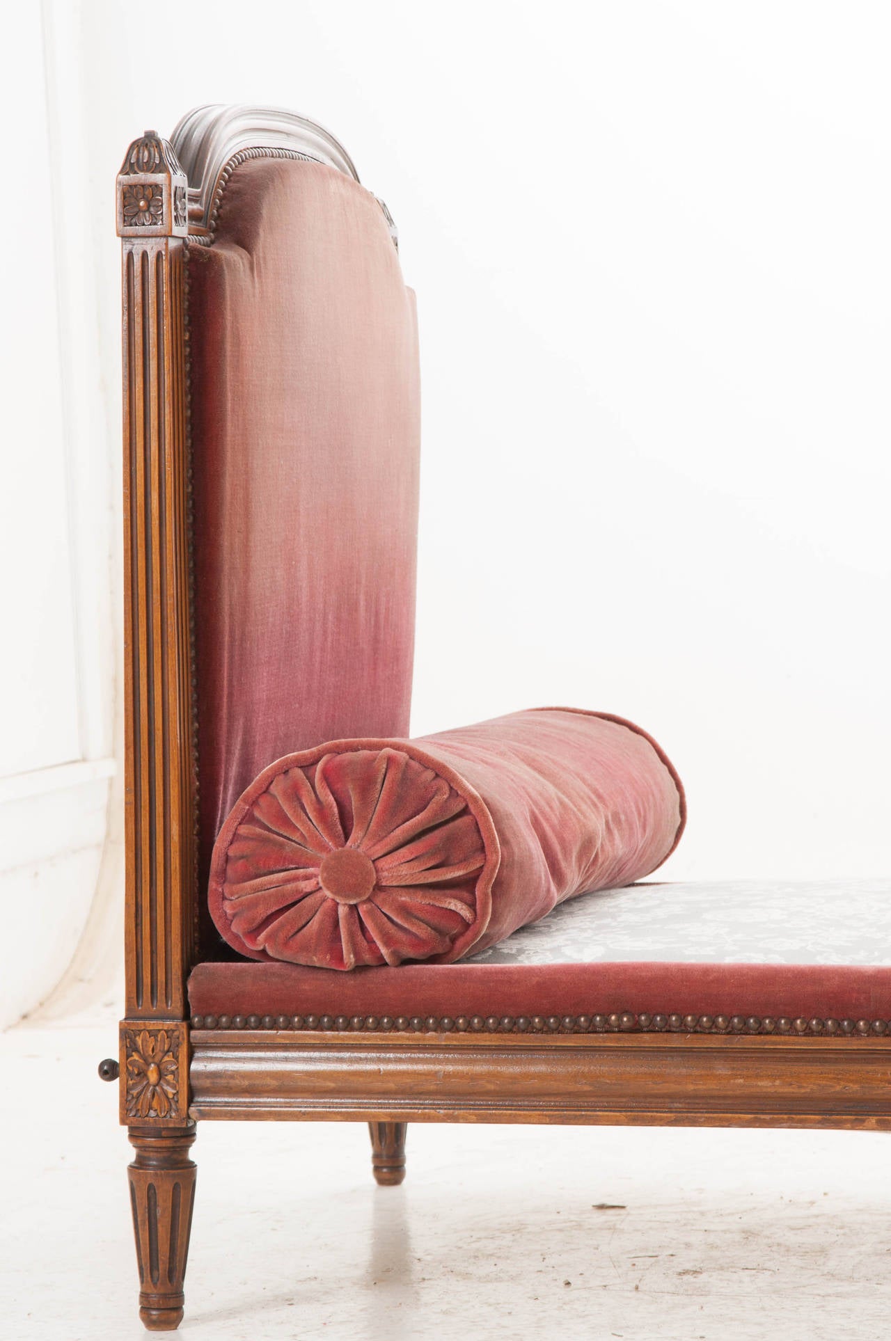 This beautiful Louis XVI  walnut daybed is upholstered in red velvet material. Notice the careful attention to detail that is exhibited in almost every inch of the beautifully hand carved walnut. Nail head trim borders all fabric. c. 1890. See