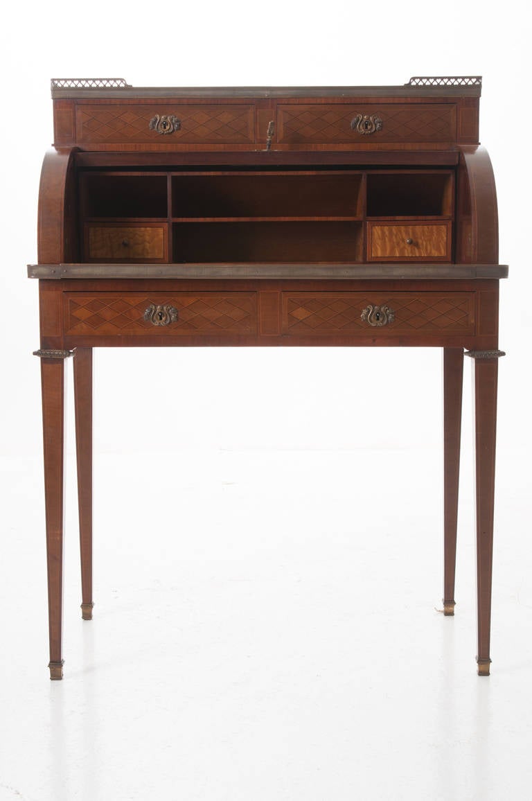 Elegant French Louis XVI lady's roll top desk of mahogany and inlay, marble top has a pierced brass gallery with two drawers below. The D roll top features diamond motif inlay with an impressive inlay crest of ribbon holding musical instruments and