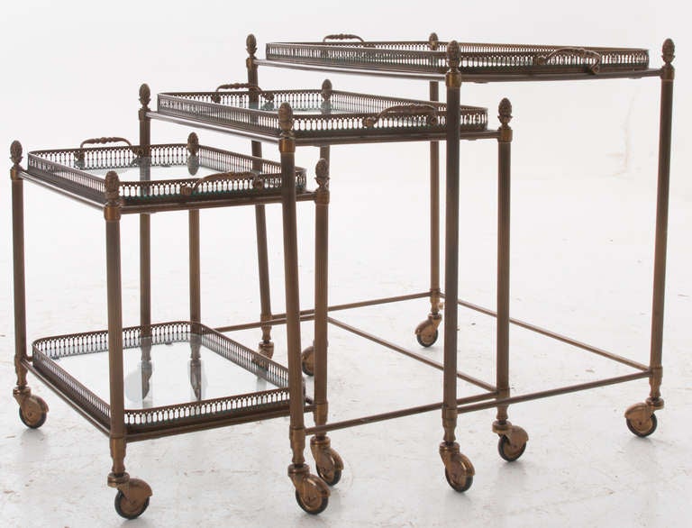 French set of 3 nesting tray tables made of brass, 4 removable trays with glass bottoms sit on the tops of each table and a second shelf on the smallest table. Wonderful versatile tables can be used in many applications, all on brass casters. 1960's