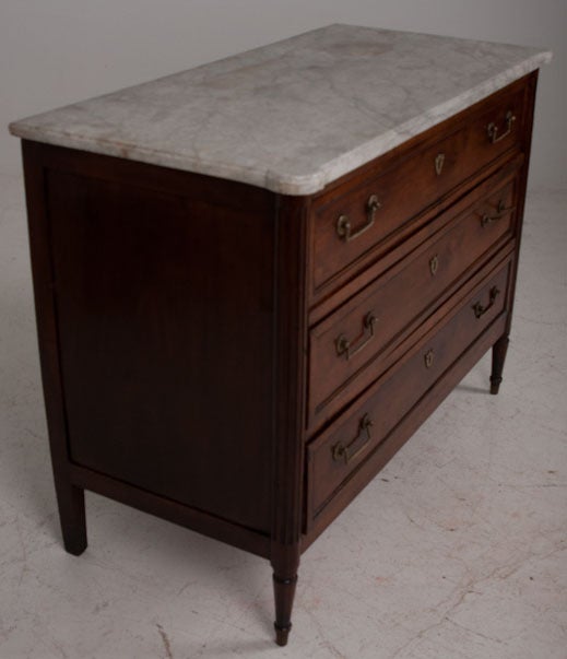 This is a wonderful old Louis XVI style walnut commode with all original hardware and old cut and shaped marble. The marble top has rounded off corners which sit over the walnut carved and fluted buffet corners.Holding in 3 large drawers with brass