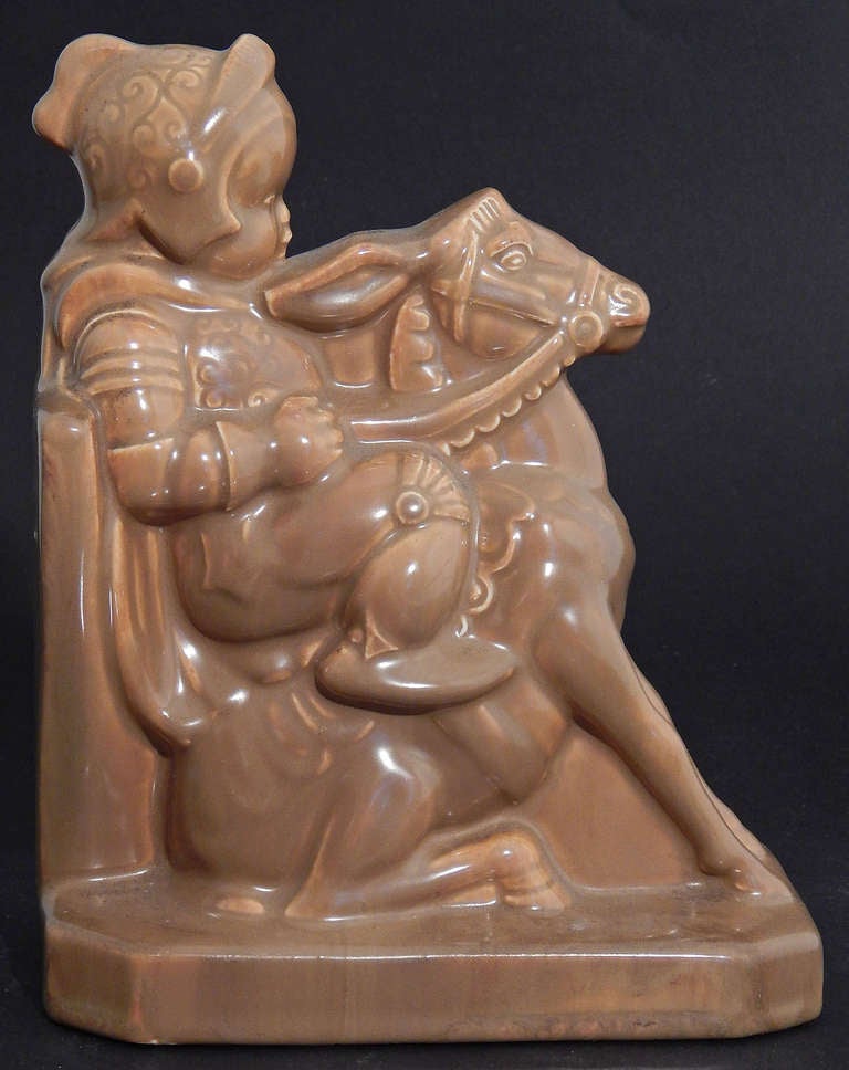 Enrobed in a delicious, rich caramel glaze, this set of whimsical yet dignified bookends depict a child knight, complete with helmet and shield, astride a donkey.  The donkey is shown with forelegs braced and ears back, while his rider seems