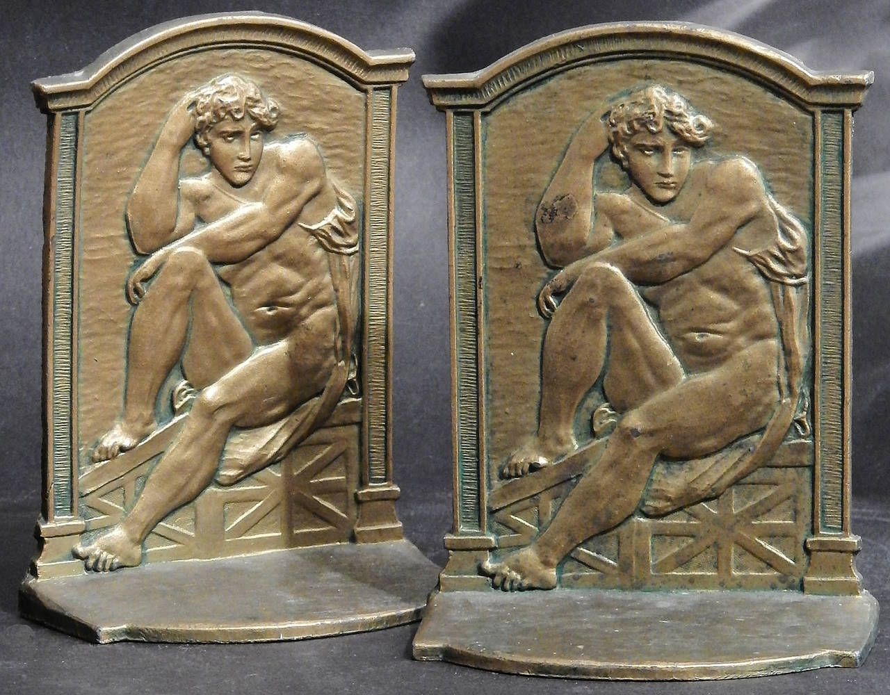 Rare and very fine, this set of bronze-toned bookends feature a nude male figure in repose, his arms resting on one knee, in a Renaissance setting topped with an arched cornice and pilasters to either side. The relief is very beautiful, and the