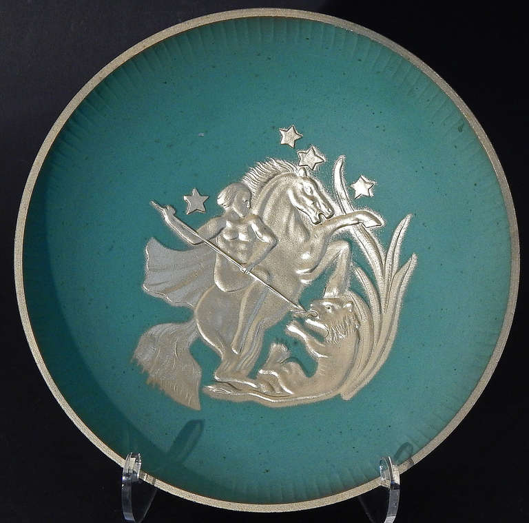 Brilliantly finished in gold and verdigris, this rare Swedish footed bowl depicts a nude female warrior on horseback spearing a lion, in bold bas relief.  The bowl was produced by the Stjärnmetall company in Sweden, probably around 1930.  The bowl
