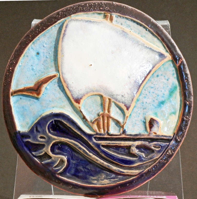 Beautifully glazed in tones of cobalt and aquamarine, this Depression-era round tile depicts two sailing ships atop a rolling sea, with a gull to one side.  The color palette chosen by the artist -- with initials 