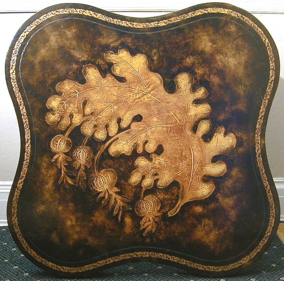 Unusual and beautifully crafted, this low table features a leaf and seed pod motif in tooled and gilded leather, the lobes of the leaf form echoed in the curves of the table.