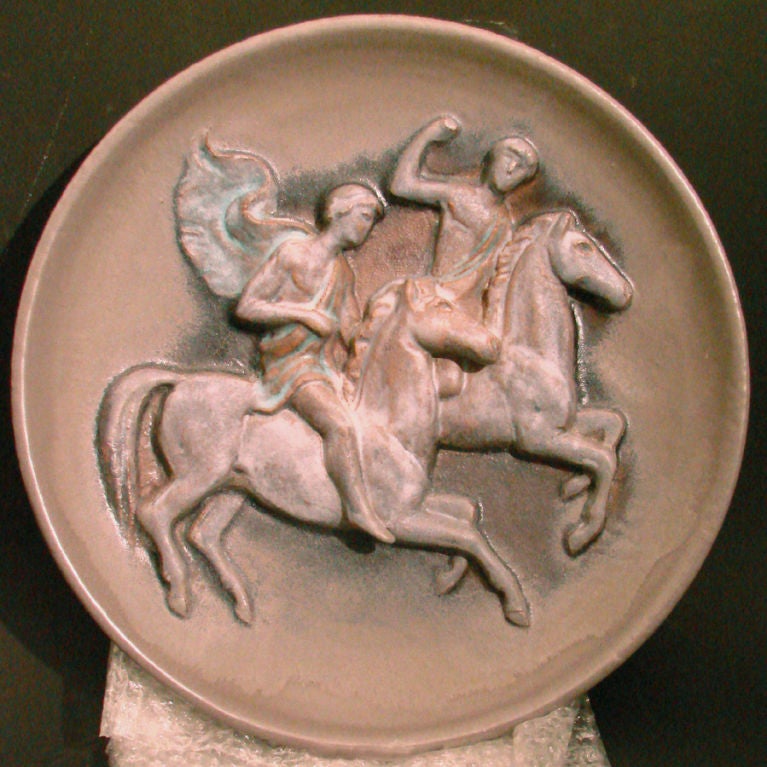 Hand sculpted and gorgeously finished in a charcoal gray glaze with undertones of blue and terra cotta, this large charger depicts a pair of toga-clad male figures on horseback.  The figures are executed in high relief, and the classical theme
