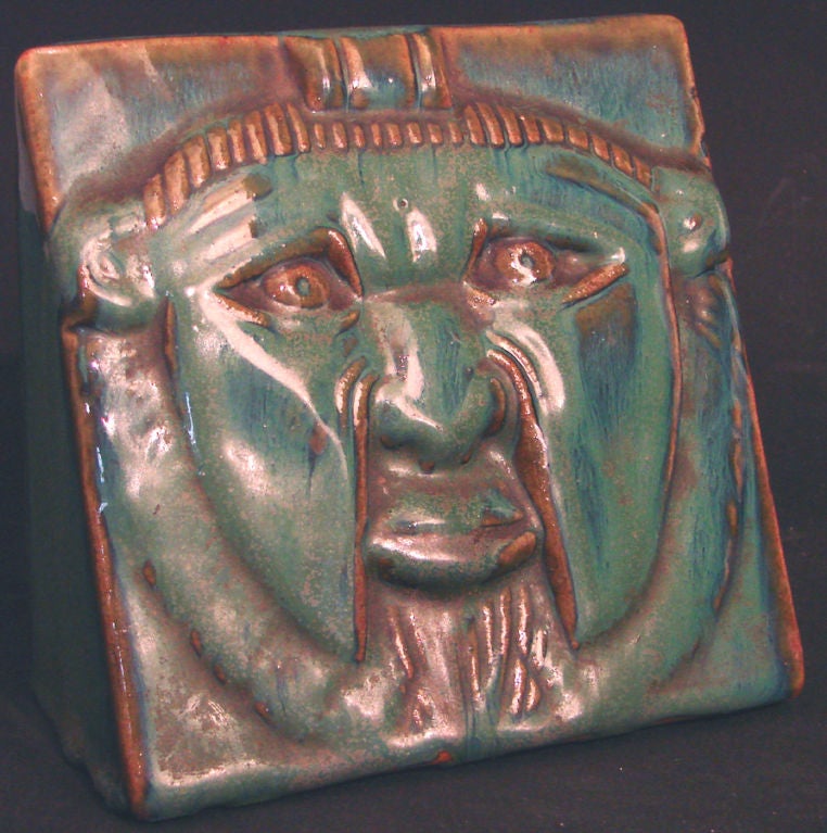 Gorgeously glazed in streaky hues of blue, green and burnt sienna, this rare, wedge-shaped bookend by Fulper Pottery features a mask-like face in bas relief.  Wedge-shaped and heavy, this piece was designed to serve as a bookend.