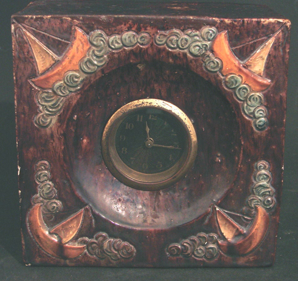 Clairement sculptée et émaillée à la main, cette merveilleuse horloge présente une série de voiliers au milieu de vagues ondulantes, chacun avec des coques dorées et des voiles ivoires vieillies.  La teinte rouge foncé tachetée de la glaçure de fond