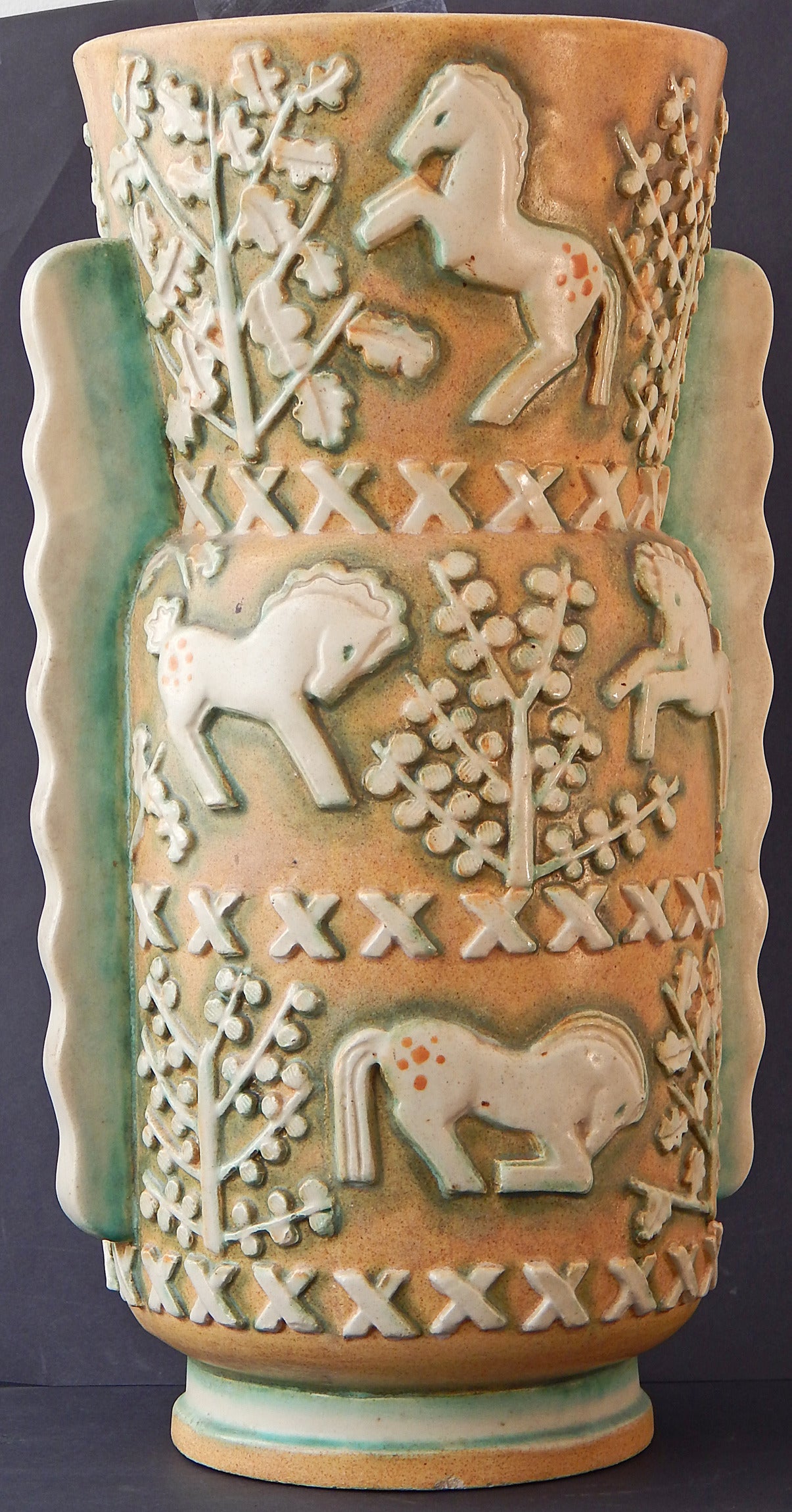 Rare and highly sculptural, this Belgian floor vase 17 inches depicts spirited ponies cavorting in a stylized Art Deco forest, executed in gorgeous creams and burnt sienna, flanked by undulating fins to each side tinged in a lovely pale green. The