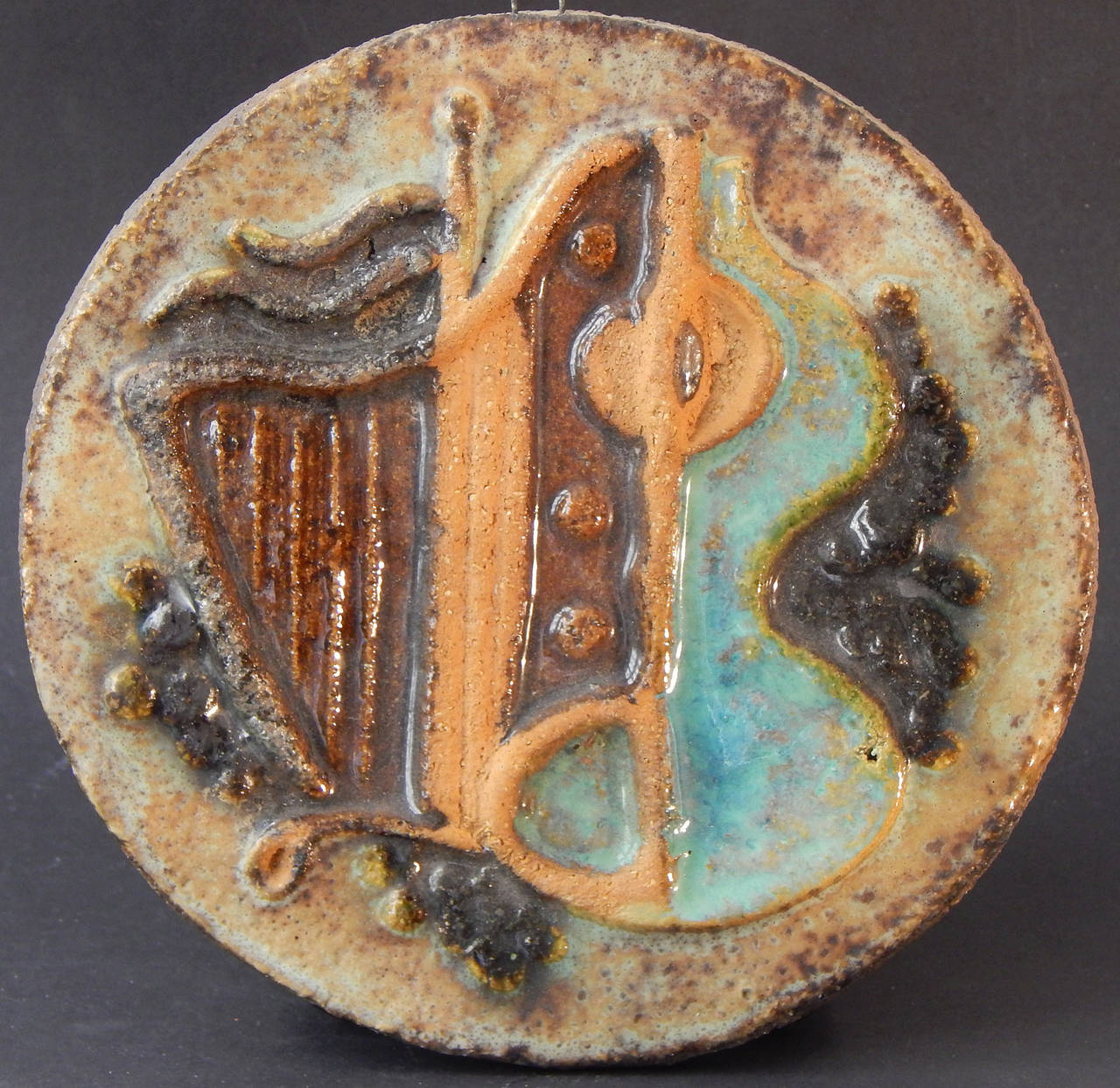 Superb in conception and execution, this pair of terra cotta plaques, depicting the pairing of a harp and guitar in the manner of Gris or Braque, is beautifully glazed in hues of turquoise, mossy green and rust.  Meant to be hung on a wall or placed