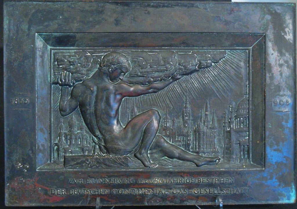 A very rare and sensuous bronze panel, this sculpture by Paul Peterich celebrates the 50th anniversary of a gas utility in Germany.  Surrounded by the towers and domes of the nation, Peterich's allegorical nude male figure is probably a reference to
