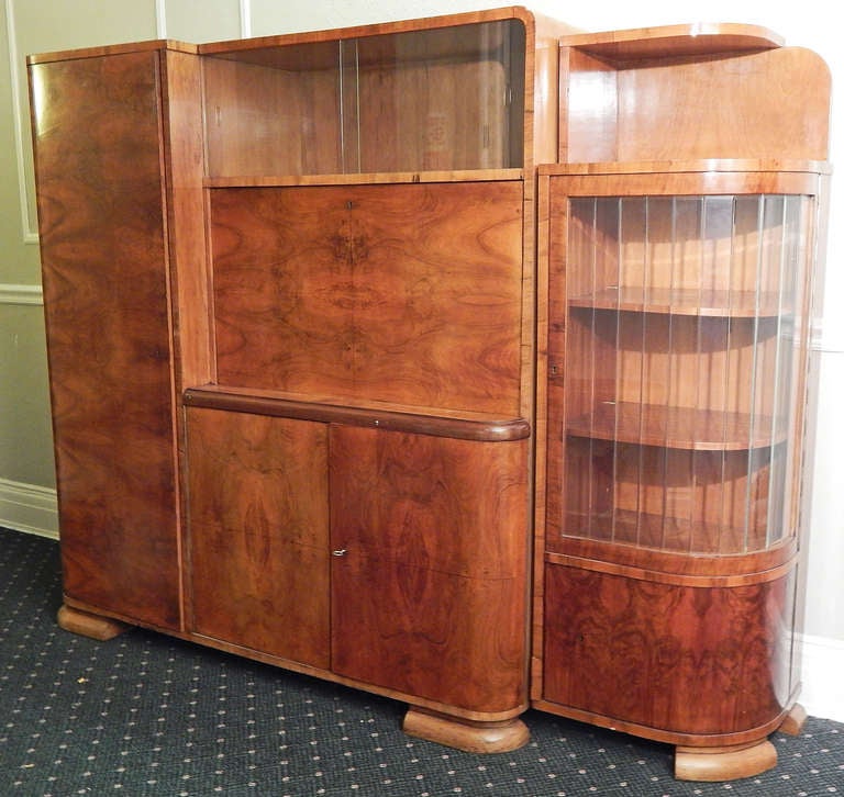 This very fine wall cabinet, complete with fold-out desk and six separate areas for storage or display, is a Fine example of late Art Deco/Moderne style and Czech craftsmanship. Finished in a highly figured reddish walnut, some of it burled, the