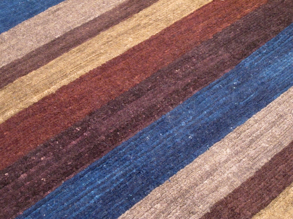 In Bolivia and Peru the Aymara people craft strikingly beautiful striped blankets and ponchos from indigenous natural materials. This carpet evokes the spirit of those Aymara stripes, anchored in deep blue with aubergine.