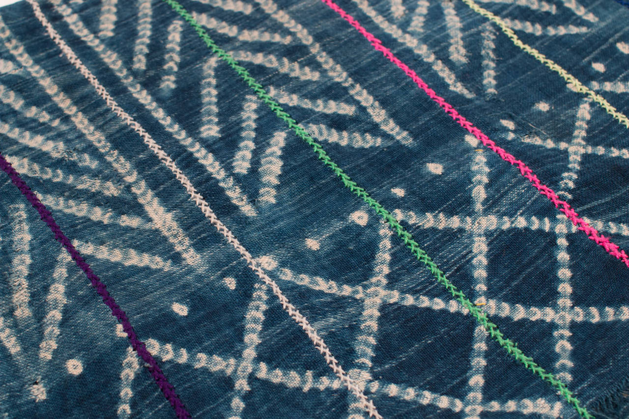 This textile is made from strips of indigo dye resist fabric sewn together and embroidered with colored yarns.