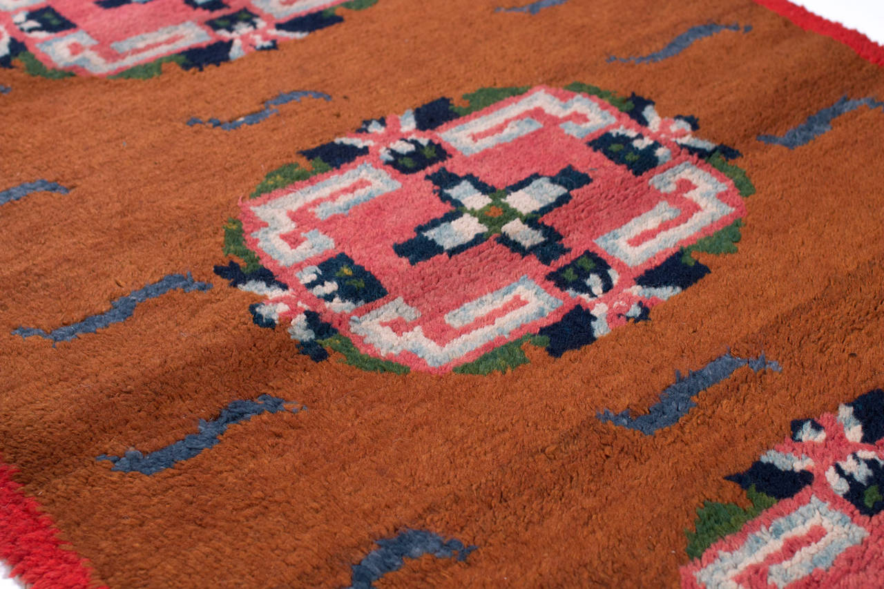 An early 20th century Tibetan rug with beautiful natural vegetable dyes. The orange field is contrasted by indigo, white and pink details. This incredible rug is handwoven with lustrous silky wool. This antique carpet is a rare and beautiful carpet