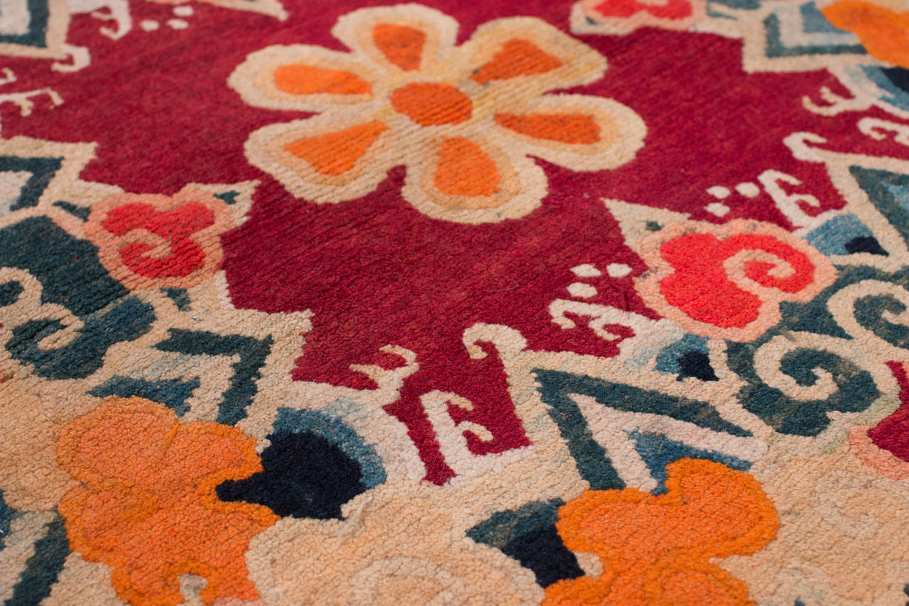 This rug is made from very silky Tibetan high-land wool. The design shows clouds and water and mountains encircling a simple geometric floral form. The edges are bound with the original Tibetan fabrics sometimes used to serge these rugs.