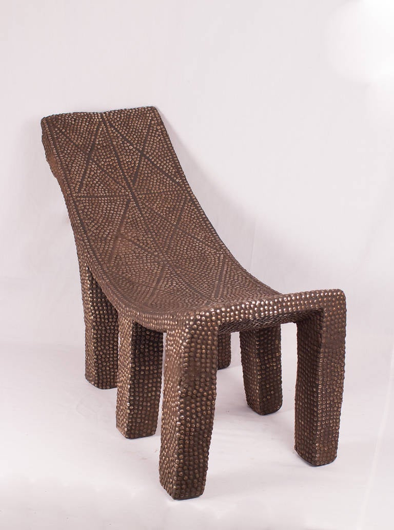 This six-legged chair comes from the Ngombe Tribe and is called the Ekele chair. It is adorned with brass and iron tacks. Ekele chairs are used as prestigious chairs meant to represent a throne for a high political, social status. Surprisingly