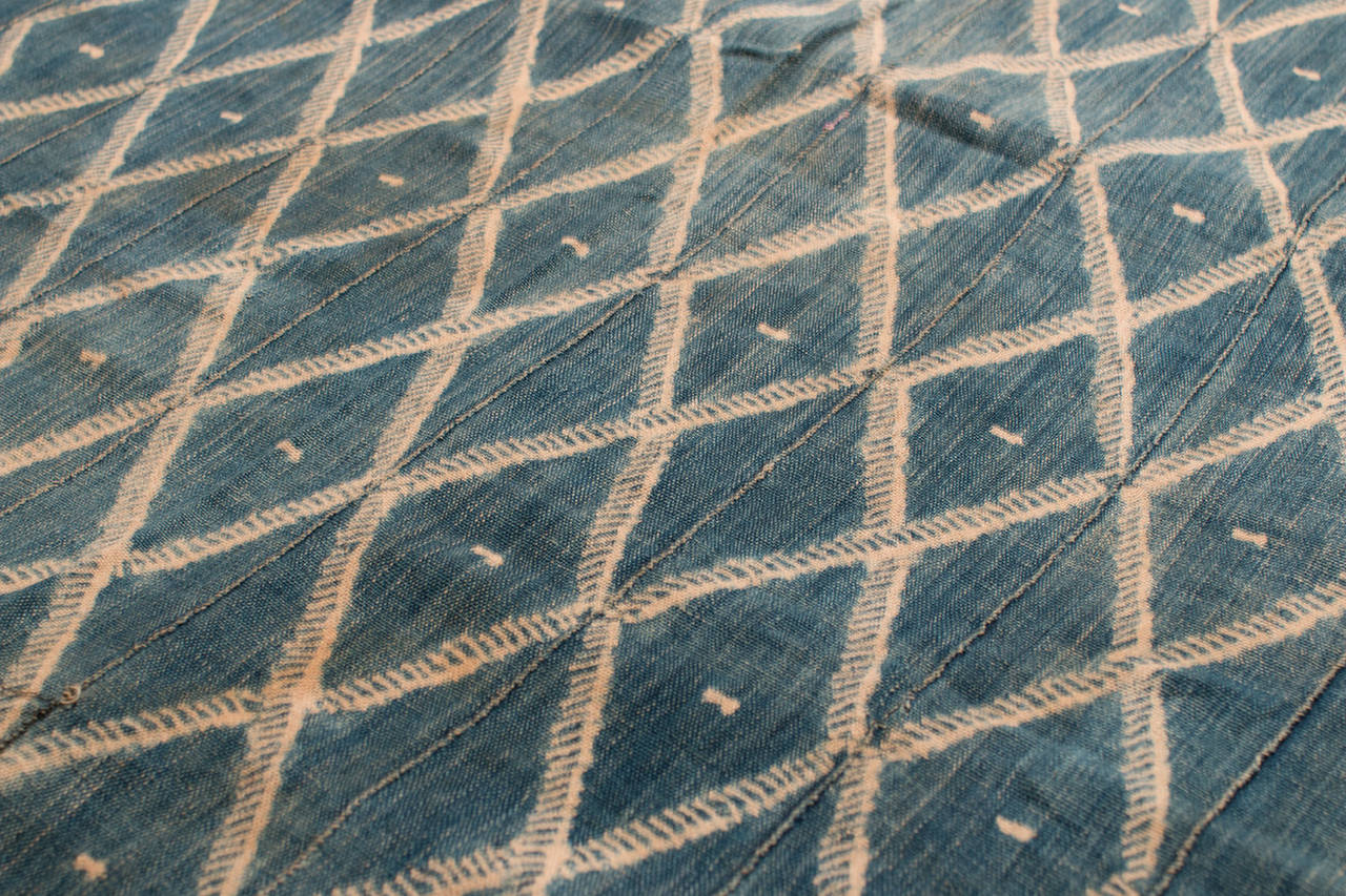 This vintage African indigo textile is from Ghana or the Ivory Coast, circa 1960. The indigo dyeing is quite beautiful with a lighter blue field color and a symmetrical diamond pattern in the center.