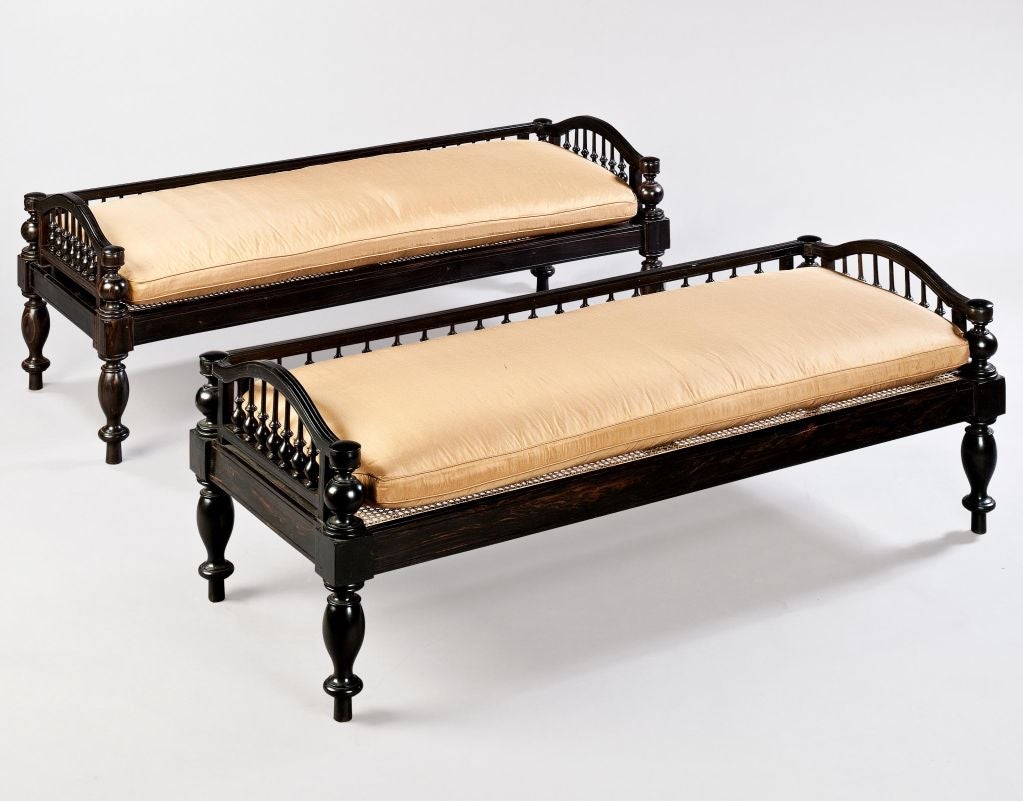 A pair of Anglo Indian ebony day beds, the upper section with a balustraded back and arched balustrades to the sides surrounding a caned seat supported on baluster turned legs. Now with cushions uplholstered in a tobacco coloured silk.