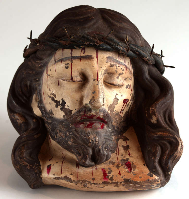 A sculpted and painted terra cotta bust of Jesus Christ at The Crucifixion, complete with a crown of thorns over flowing hair, blood droplets on the face and neck, eyes closed.