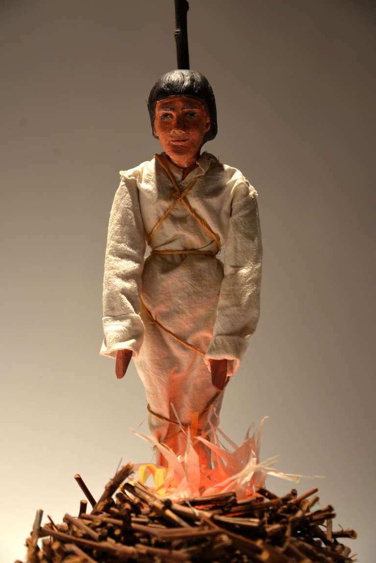 A marionette has been reconsidered here, lashed to a stake and mounted over a lighted pile of sticks  with a low-watt glow bulb and faux flames which flicker when plugged in.   A small fan engages when plugged in, creating the fire pit.