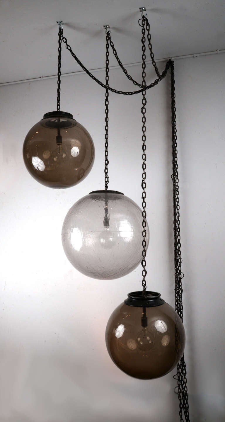 A matched pair of two 18 inch diameter smoke-colored globes and one single 21 inch globe with a textured, frosted look, all on custom chain swags with custom-made socket assemblies and cloth-covered cord.