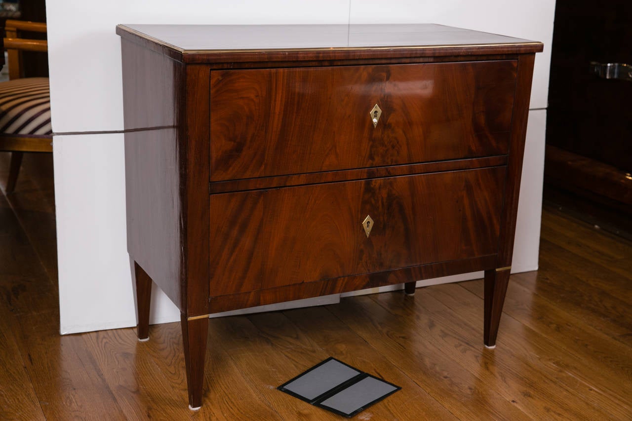Beautiful 19th century Continental pair of two-drawer chests on high tapered legs in mahogany veneer with brass escutcheons and trim detailing, recently restored and refinished.