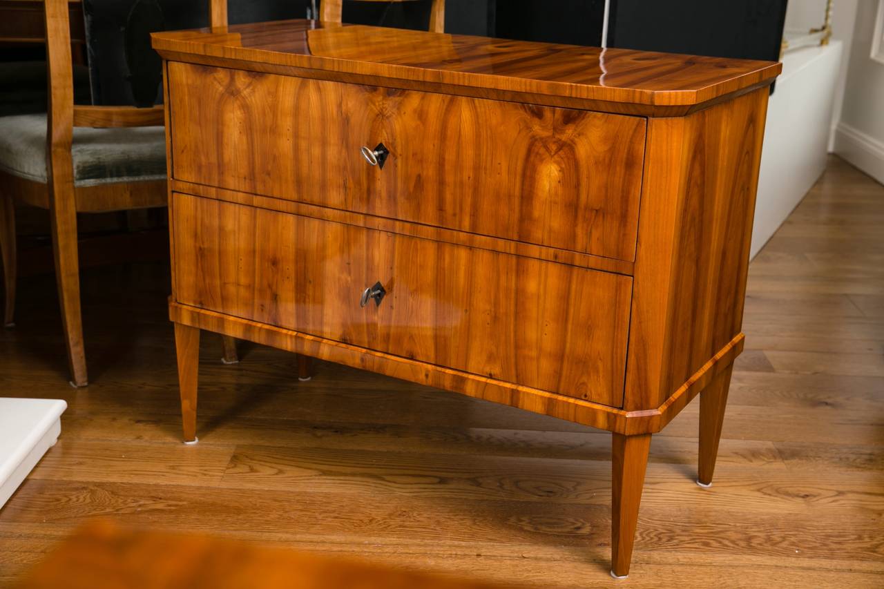 Wonderful pair of sleek early Biedermeier blonde cherry veneered two drawer chests with chamfered edges finishing on angled straight, tapered legs.
Note exquisite movement of the book matched veneer.