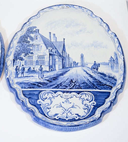 Provenance: From the collection of Katherine Mellon
A pair of large Delft Blue and White oval plaques showing countryside scenes within a shaped border, one with a village riverside scene, the other with a village pastoral scene.
Enamel decorated